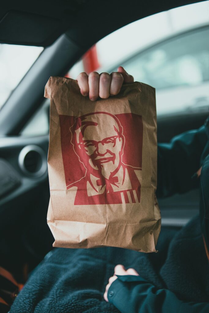 Home A person holds a KFC paper bag inside a car, showcasing fast food takeaway packaging.